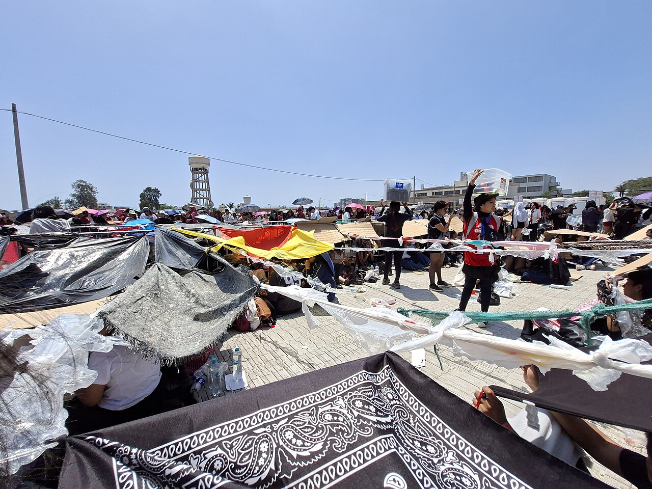 Fans wait beneath shade tarps as vendors pass through the Lima concert waiting area