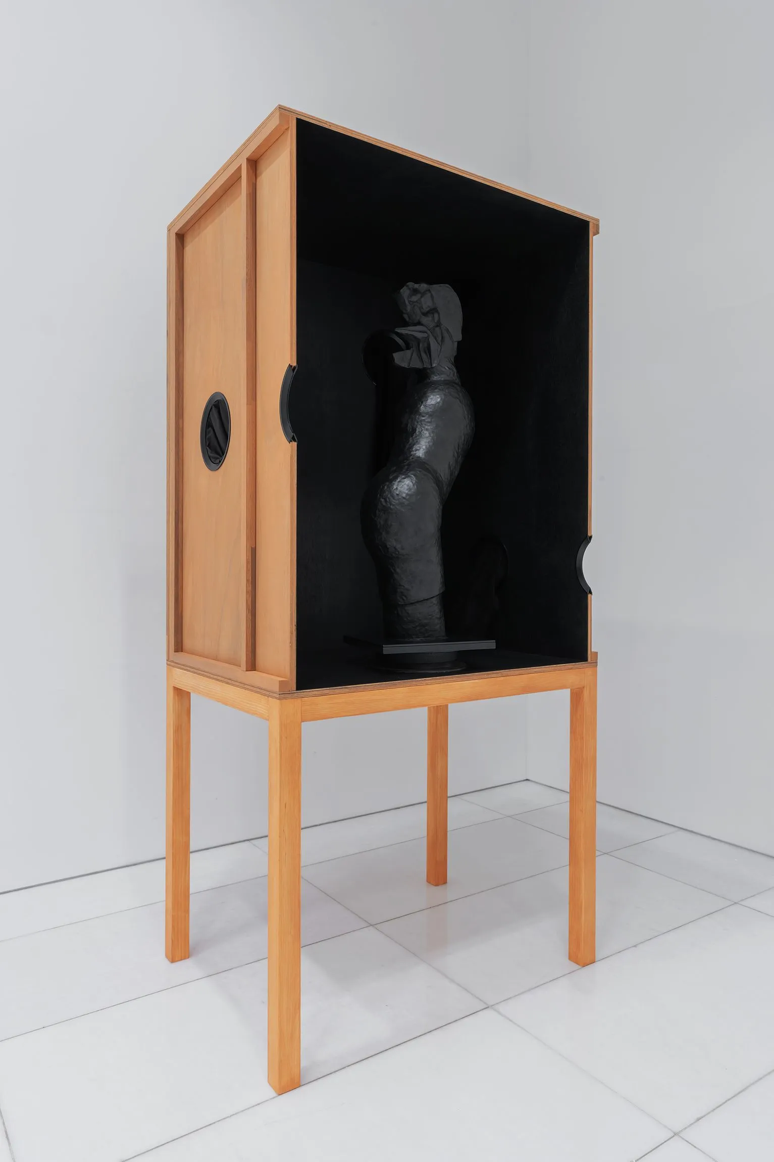 A black sculpted figure inside a wooden box on legs