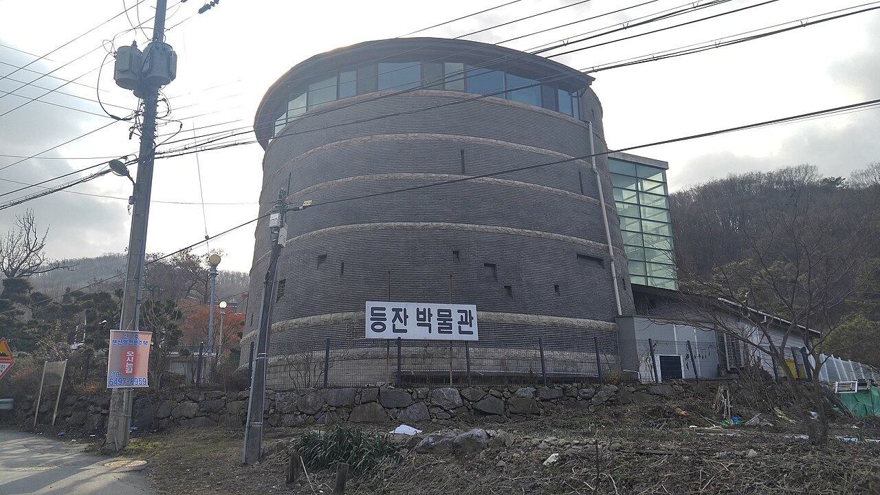 등잔박물관 간판이 붙은 둥근 벽돌 건물과 유리 계단실, 앞을 지나는 전선과 겨울나무