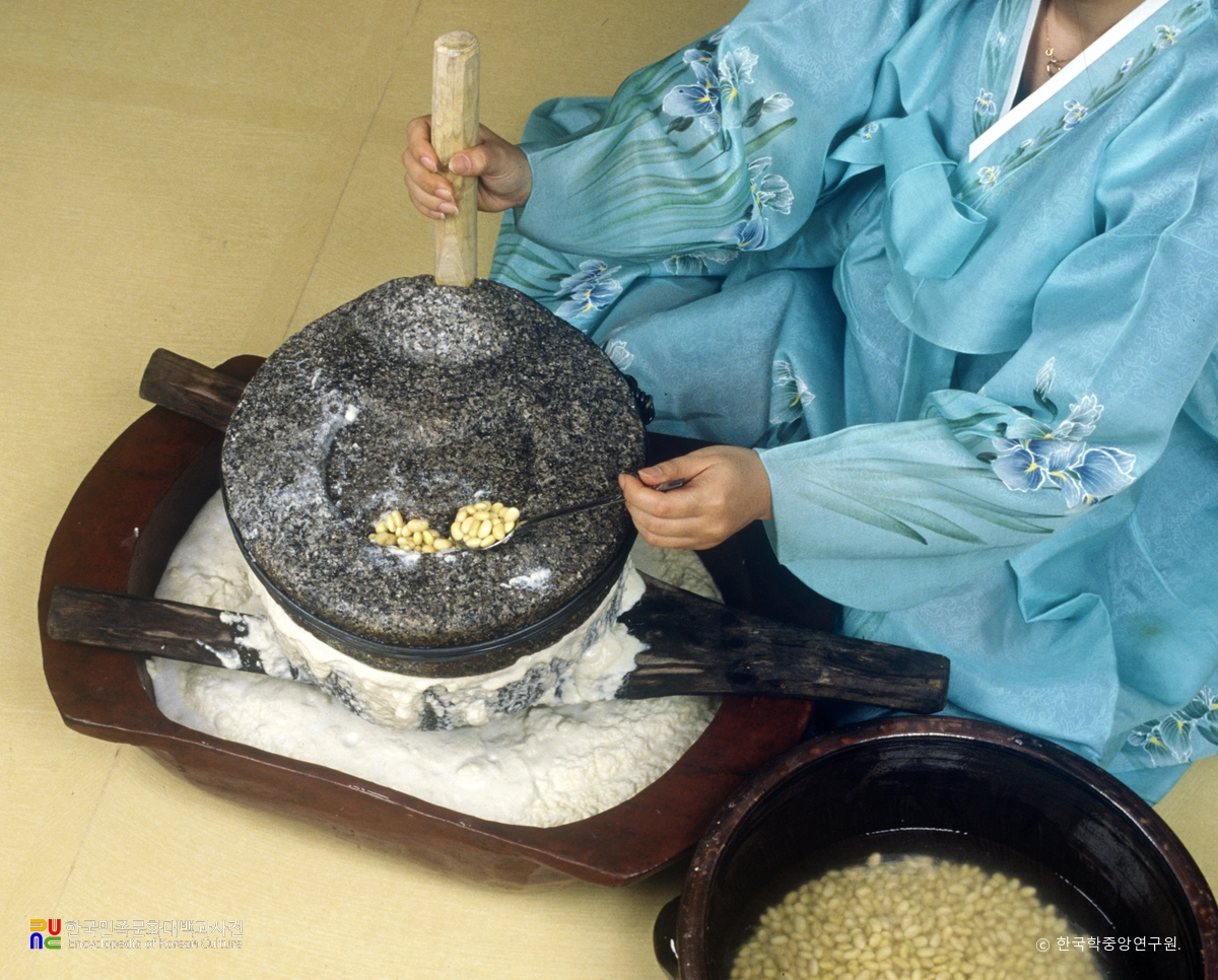 숟가락으로 콩을 넣으며 맷돌을 돌리는 모습. 갈린 콩은 아래 함지에 모인다. 촬영연도 미상.