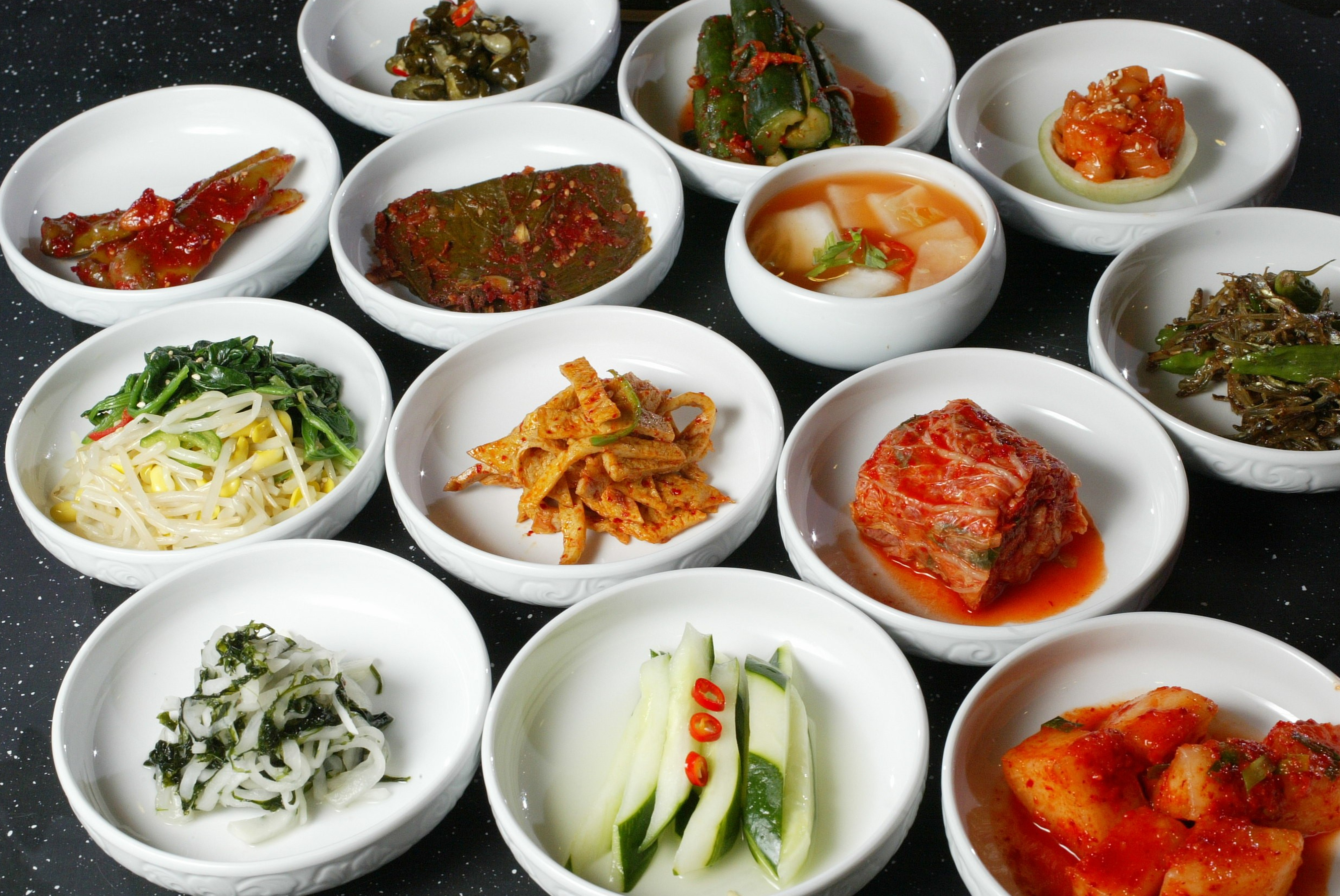 작은 흰 그릇에 나눠 담긴 배추김치, 채소 반찬과 멸치 반찬