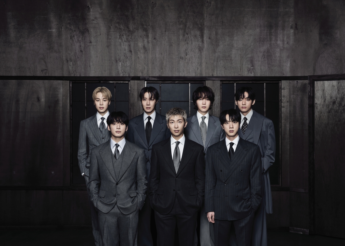 어두운 목재 벽 앞에 정장 차림으로 선 방탄소년단 일곱 멤버