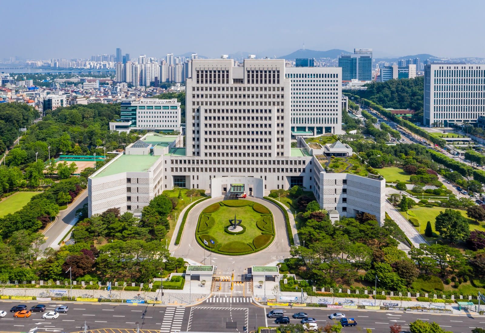 The white Supreme Court building behind a circular garden, with Seoul's skyline beyond