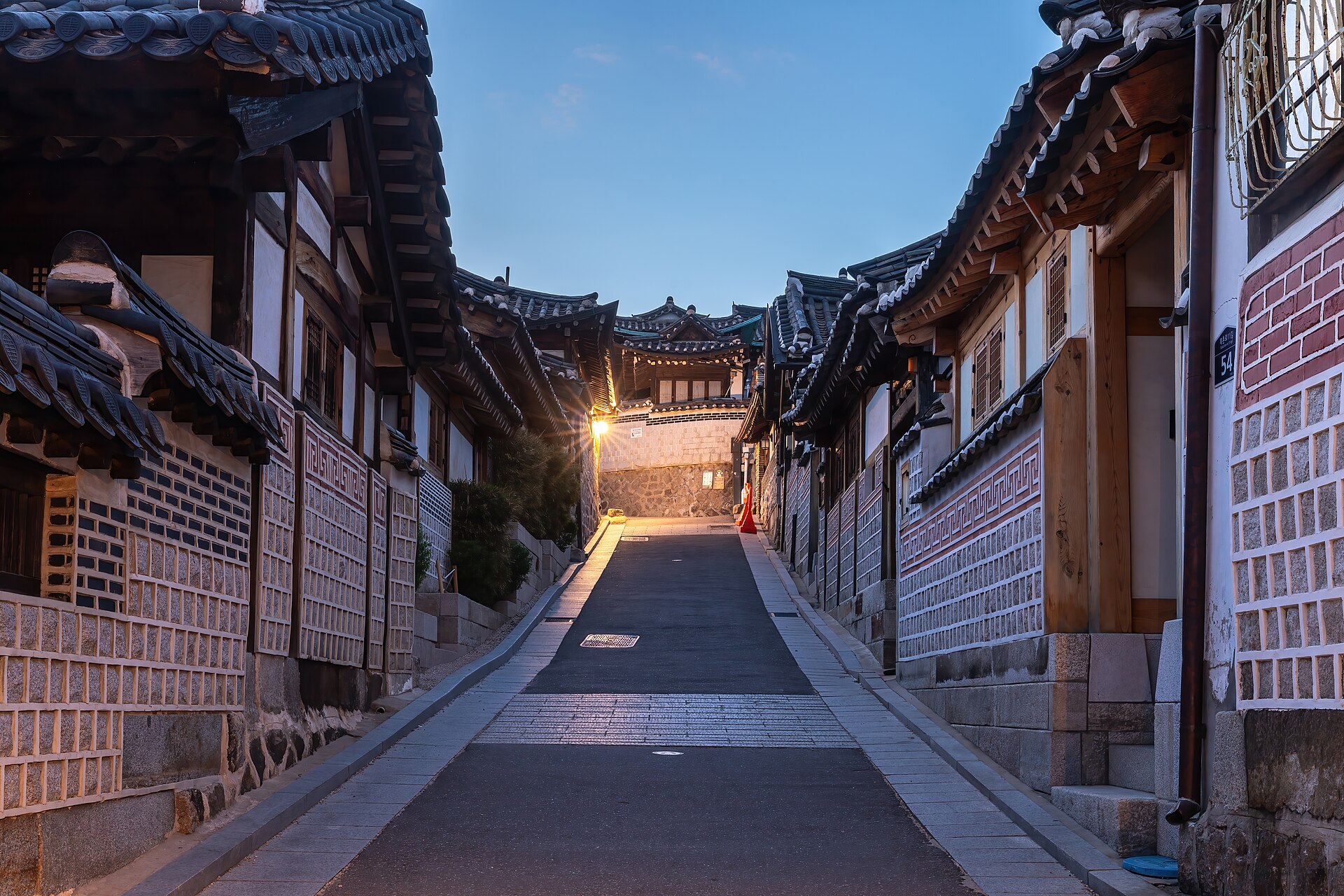 A hanok alley under a deep blue evening sky with a lit street lamp