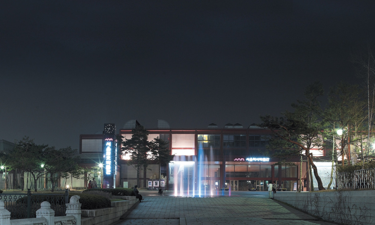 어두운 하늘 아래 분수와 불빛이 켜진 서울역사박물관 야간 전경