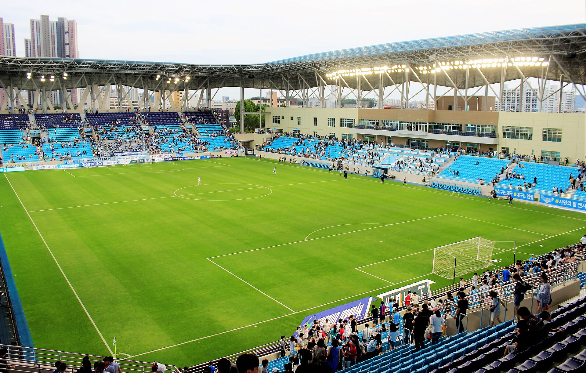푸른 관중석과 초록 잔디, 철골 지붕이 보이는 대구의 축구 전용 경기장