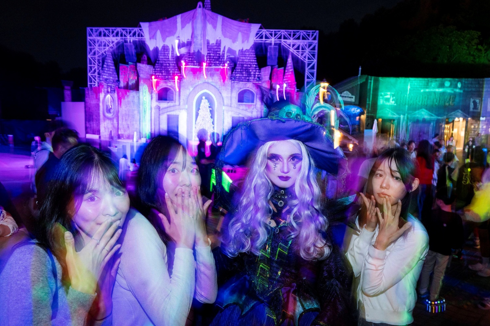 Three visitors pulling shocked faces next to a performer in a witch costume in front of a purple-lit stage set