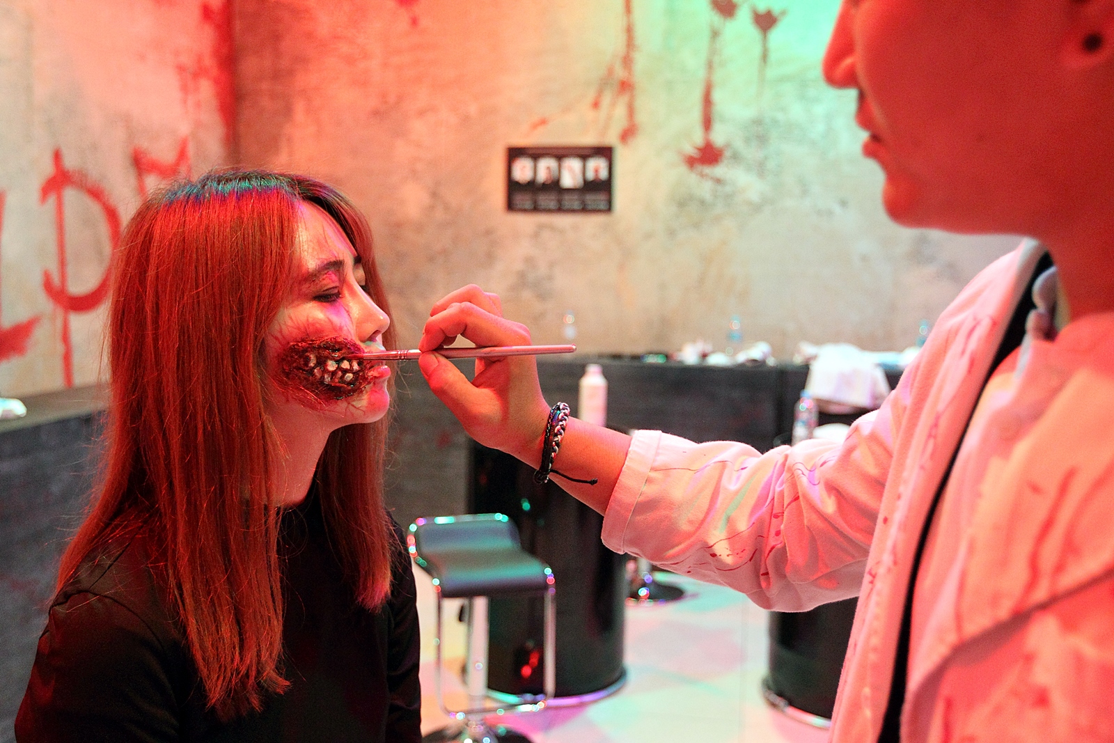 A makeup artist painting a zombie wound on a visitor's cheek