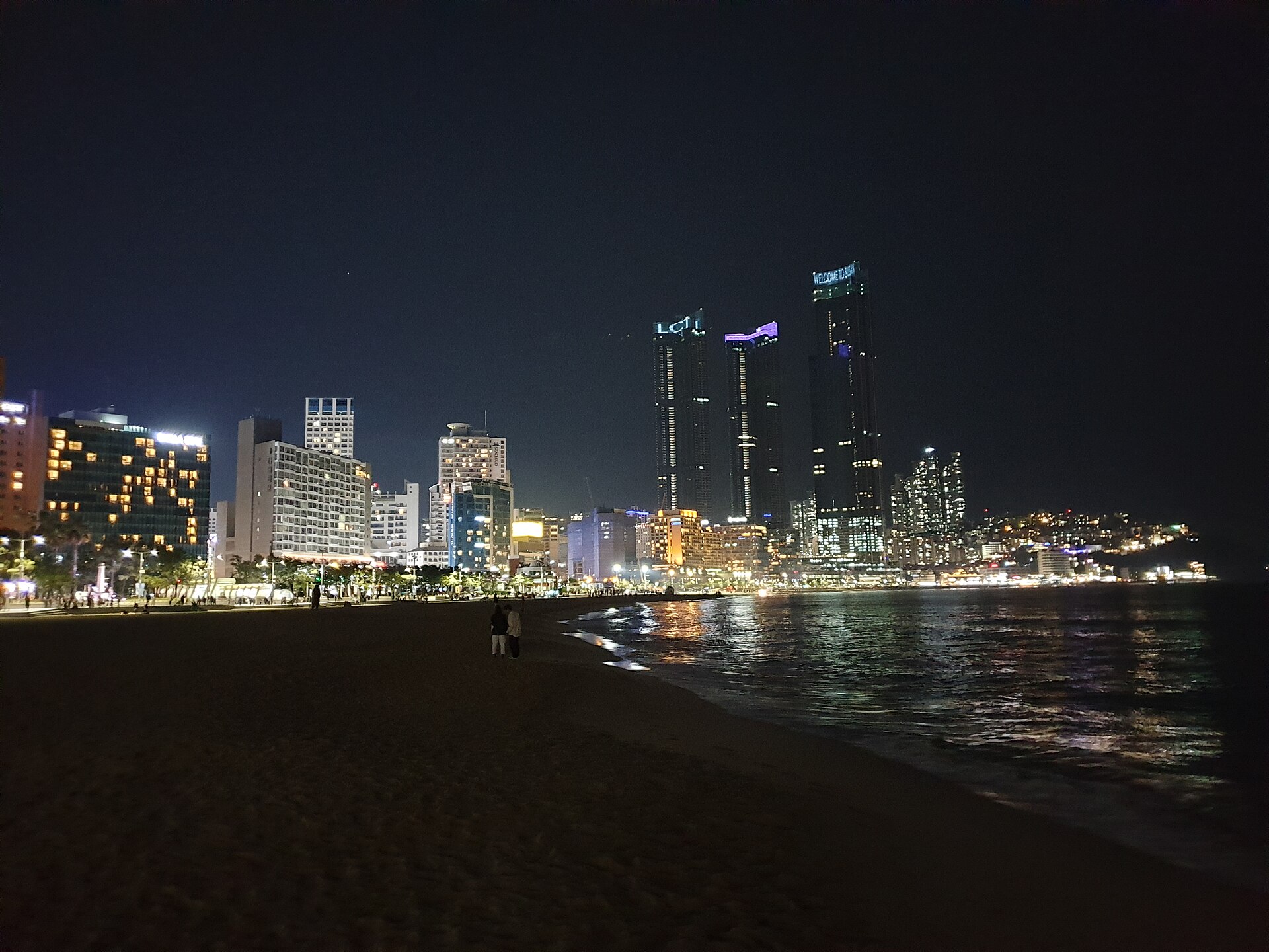 暗い海と砂浜の向こうに明かりの灯る高層ビルが並ぶ海雲台の夜景