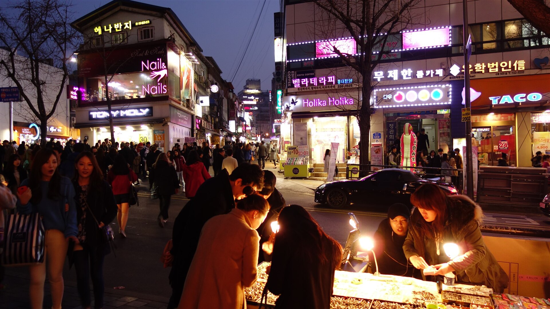 네온 간판이 켜진 저녁 홍대 거리에 사람들이 가득한 모습