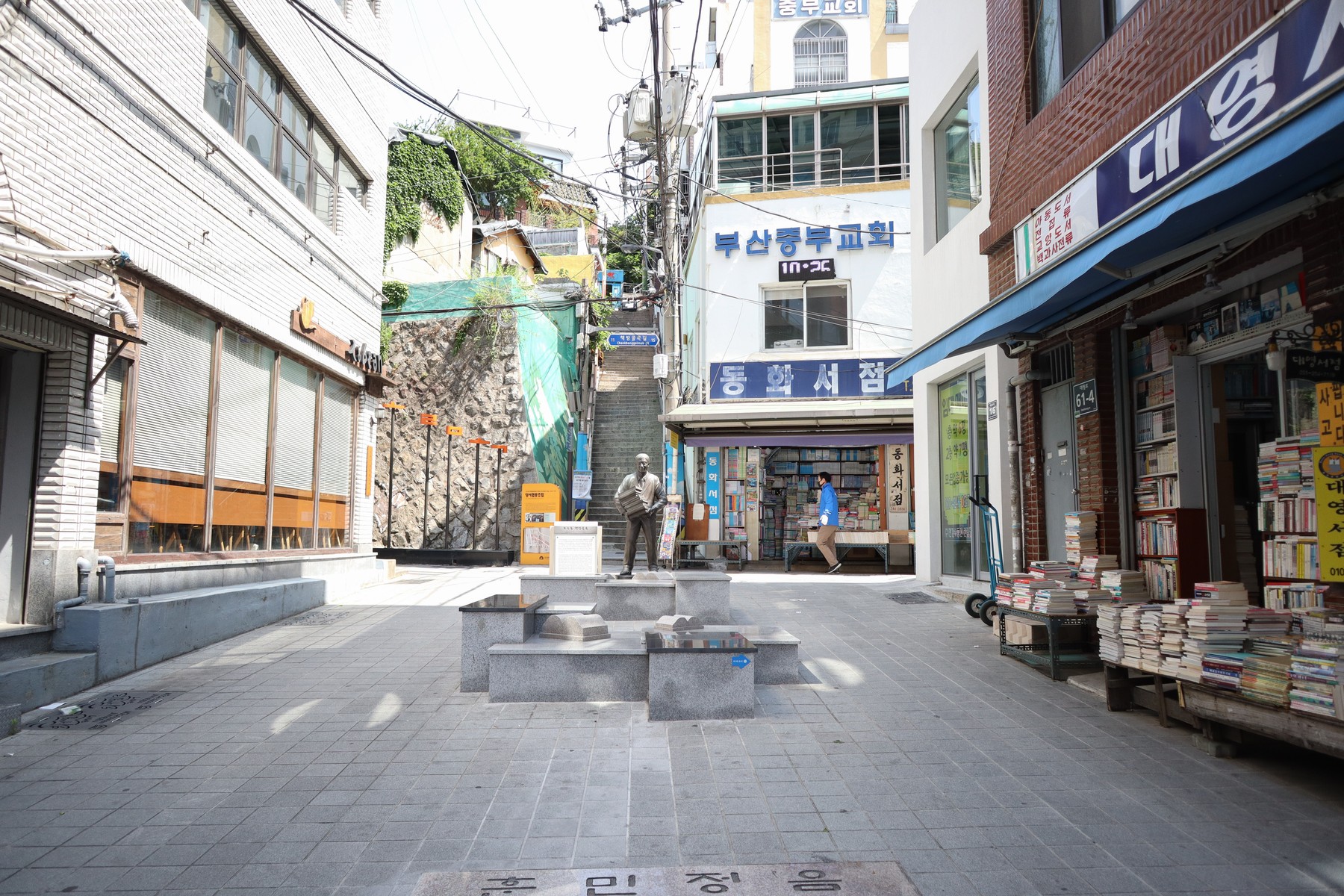 보수동책방골목의 넓어진 진입부, 중앙의 조형물과 오른쪽 서점 앞 책더미.