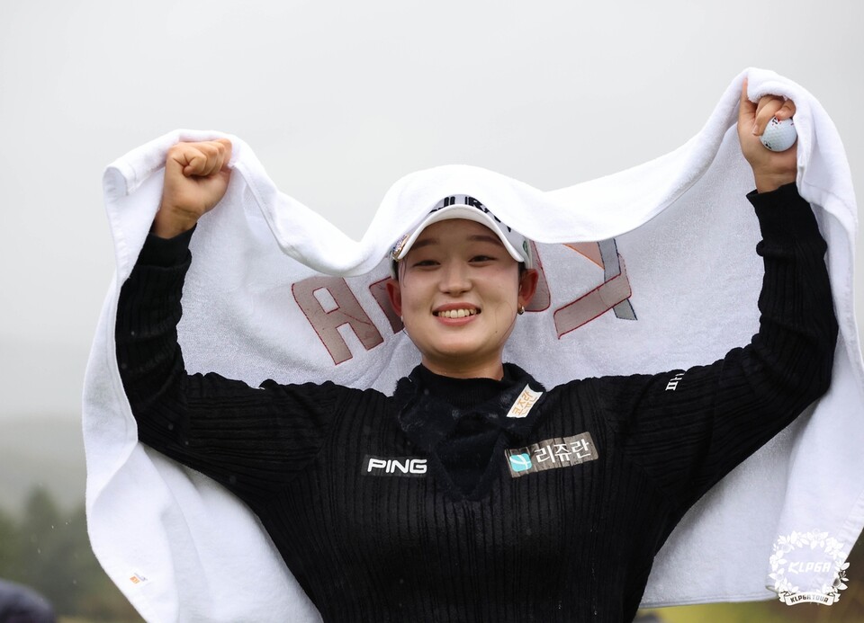 흰 수건을 머리 위로 펼치고 두 주먹을 쥔 채 웃는 여자 골프 선수