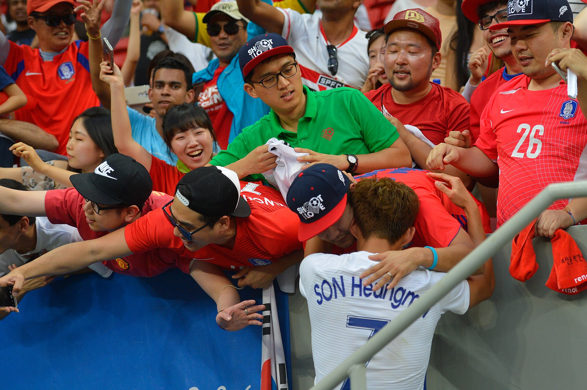 Son in a white No. 7 shirt embracing fans in red over the stand railing