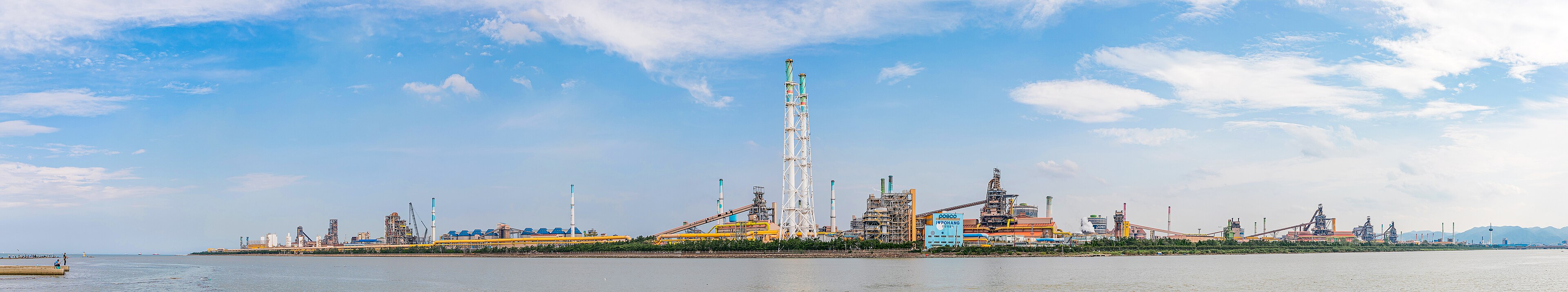 Chimneys and plant of the Pohang steelworks stretching along the shore under a blue sky