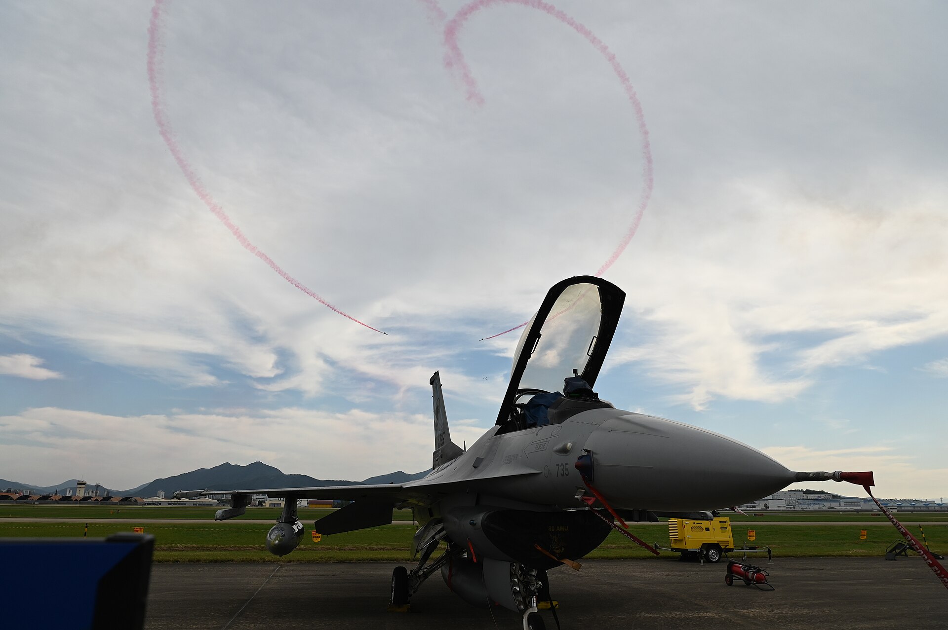 A red smoke heart in the sky behind a parked fighter jet