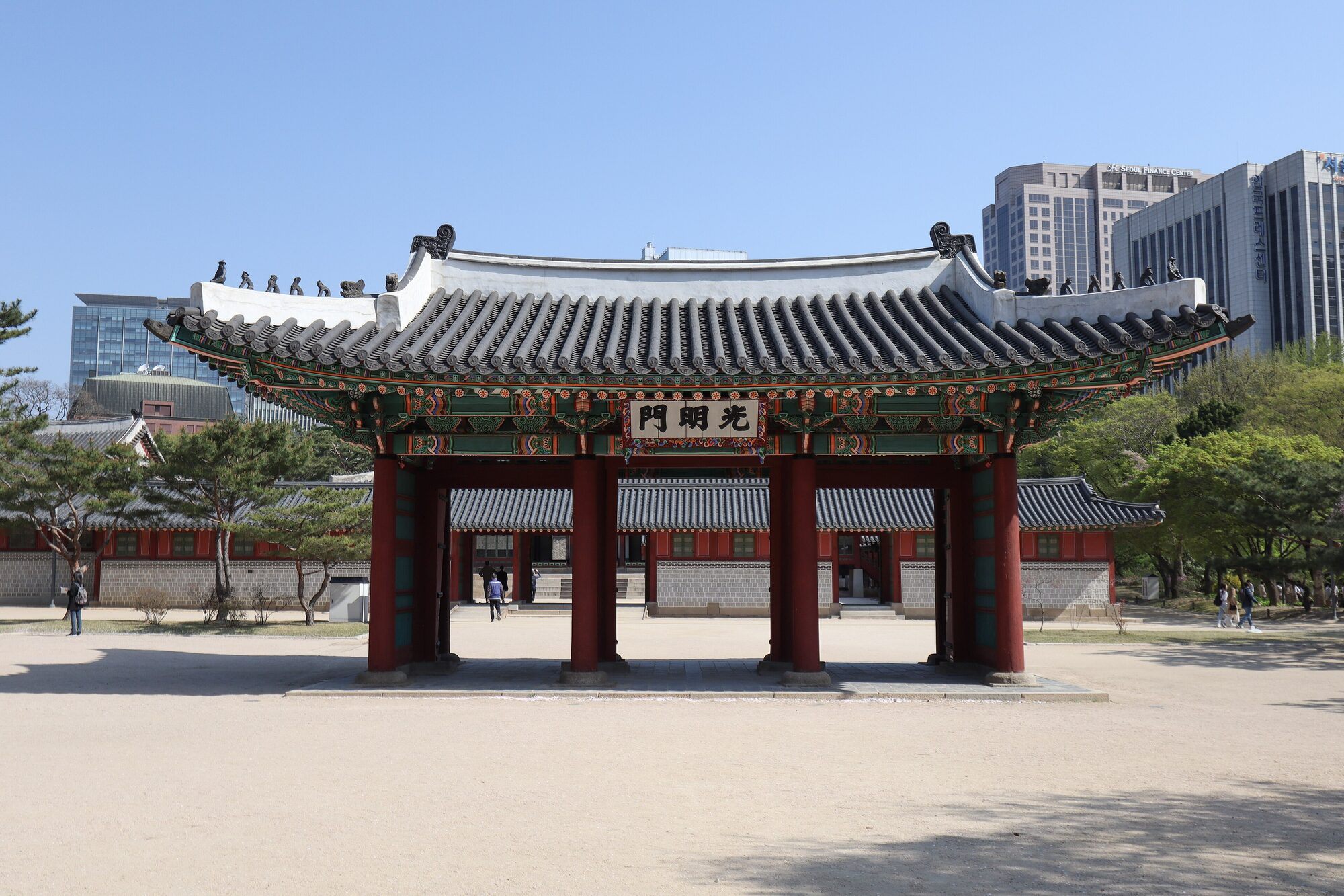 붉은 기둥과 기와지붕의 광명문 뒤로 고층 빌딩이 솟은 덕수궁