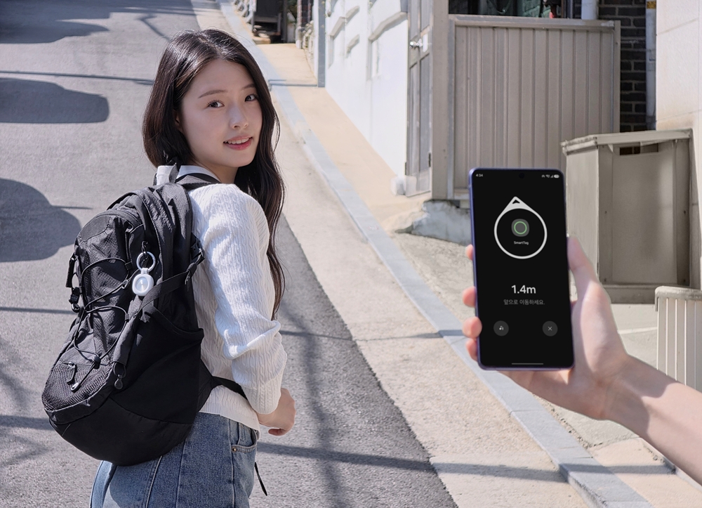 白いSmartTag3を付けたバッグを背負うモデル。手前の手が持つスマートフォンには方向矢印と1.4mが表示されている。
