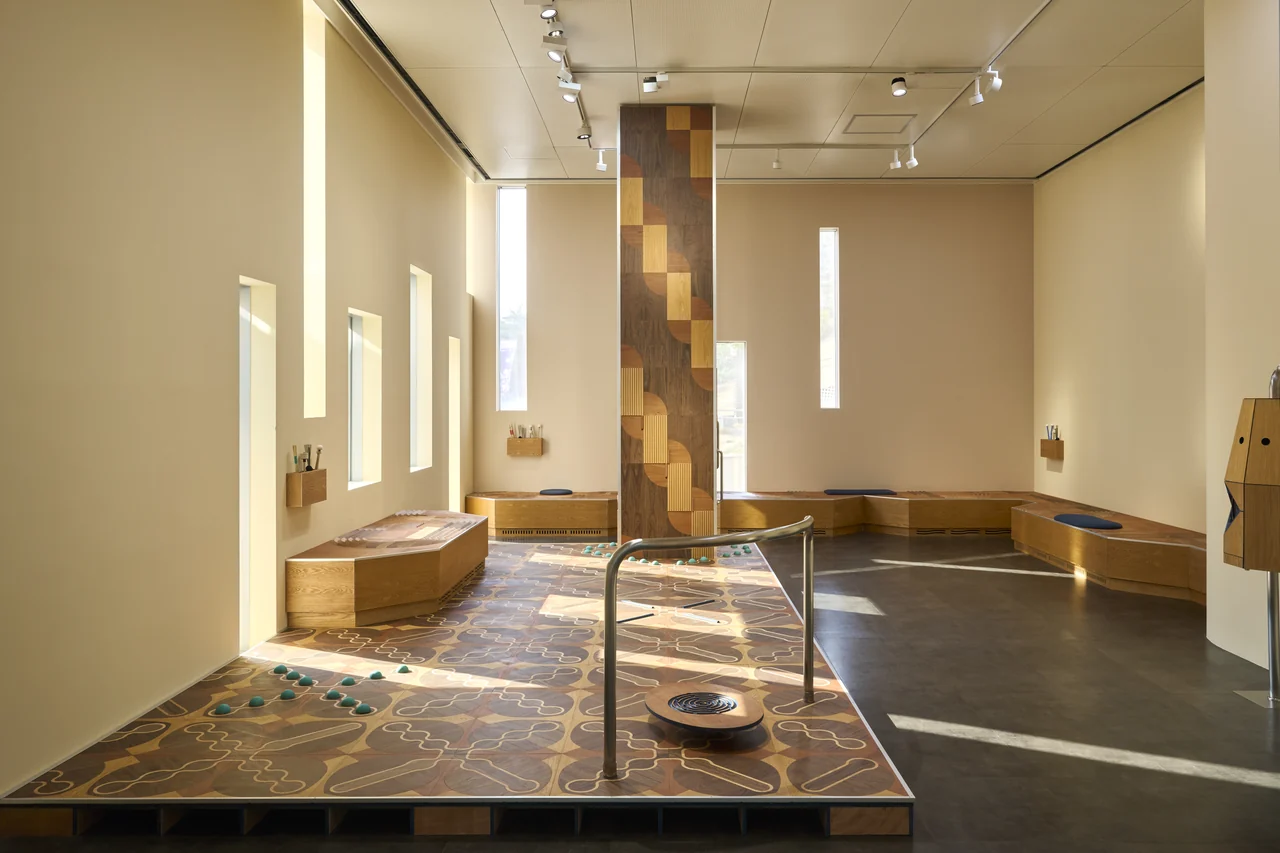 美術館のラウンジに置かれた木の彫刻とベンチ。2026年の展示風景。
