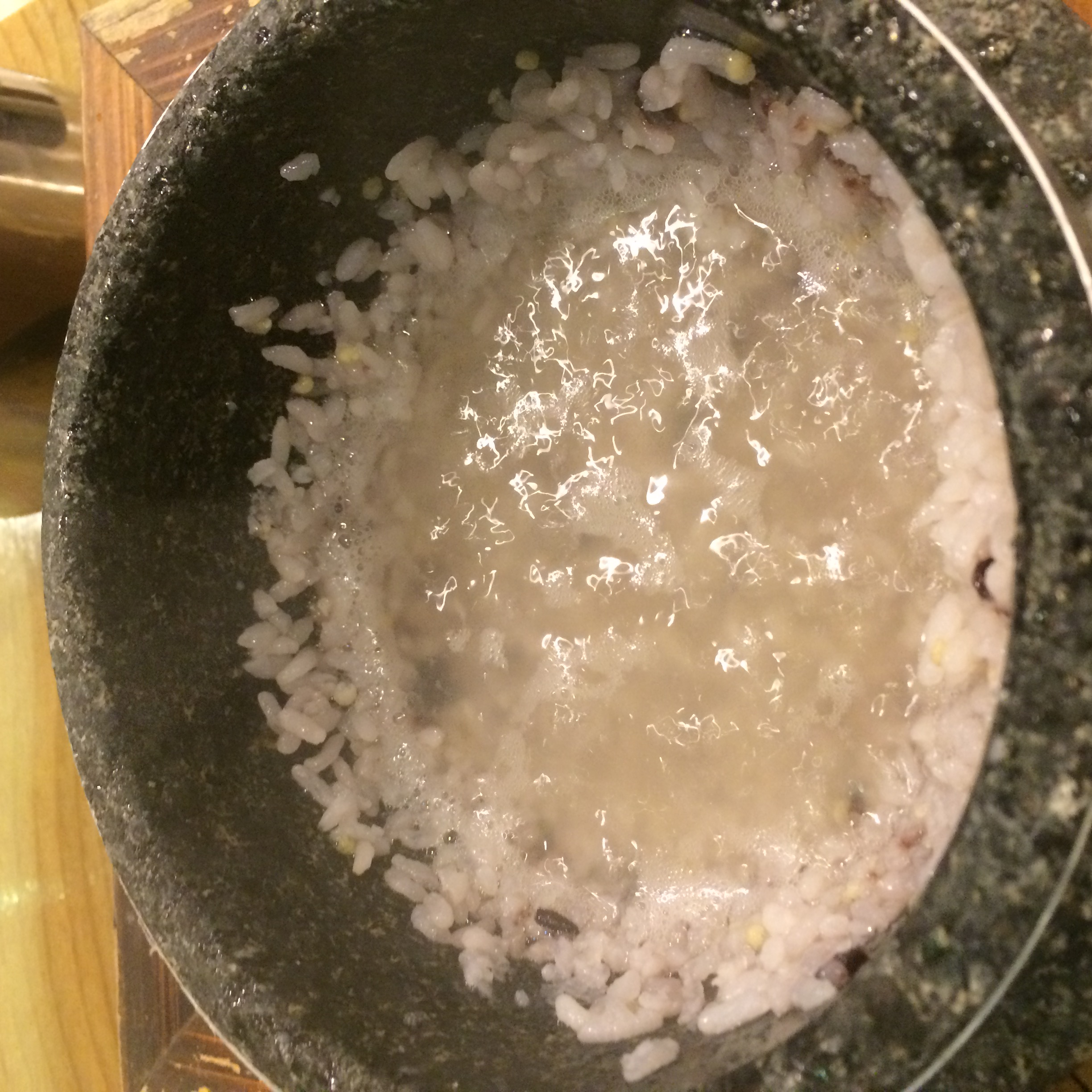 黒い石釜の内側にご飯粒が残り、中央に白く濁った水と小さな泡が見える様子