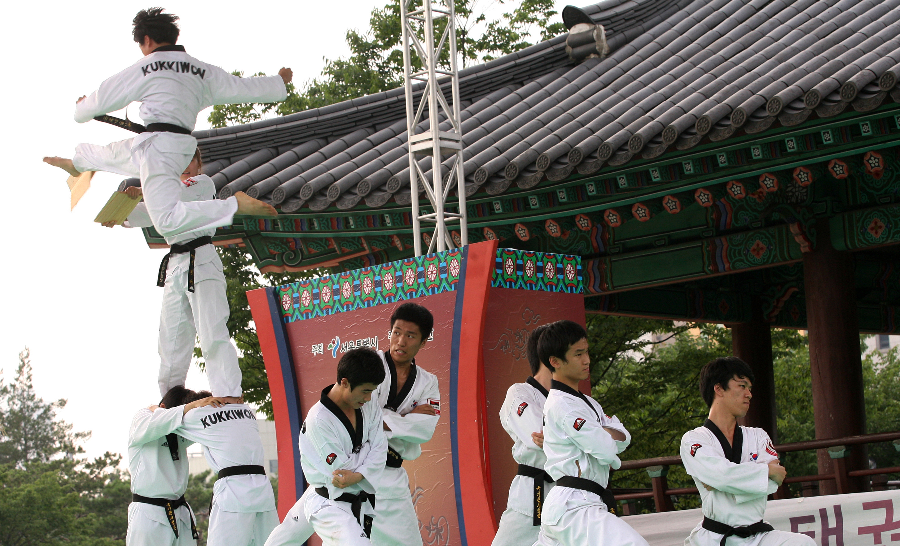 2012년 남산골한옥마을에서 동료들 위로 뛰어올라 발차기를 하는 국기원 단원과 한옥 지붕