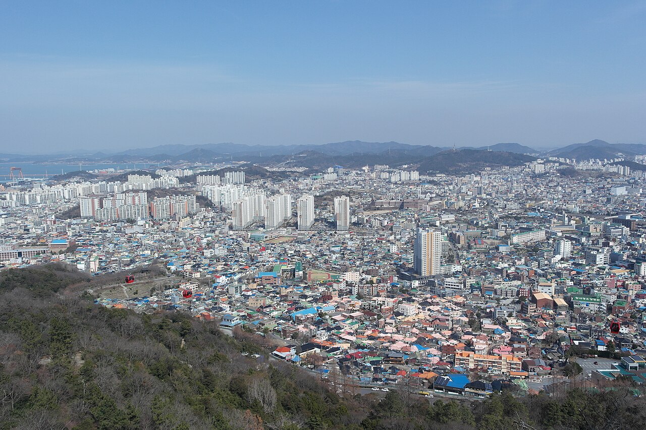 낮은 지붕과 아파트가 넓게 펼쳐지고 전경에 붉은 케이블카가 지나가는 목포 시가지