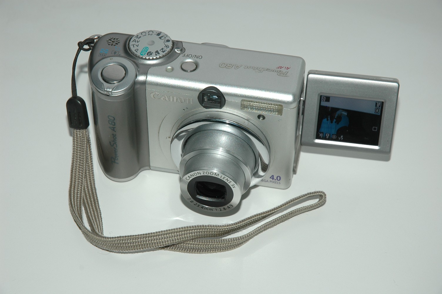 렌즈와 회전형 LCD 화면을 펼친 은색 Canon PowerShot A80과 손목 스트랩